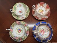 Four Paragon cups and saucers arranged on a dark wood table, showing different floral patterns and gilded details.