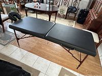 Full view of the black padded portable massage table unfolded in a room, showing the entire length and legs.