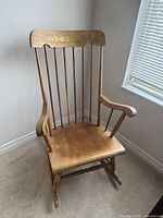 Front view of maple wood rocking chair with vertical spindles and decorative top rail.