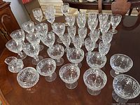 Top-down view of the entire collection of Royal Doulton crystal stemware arranged on a wooden table, showing multiple sets of glasses and two small dishes.