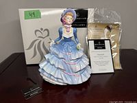 Photo of the Royal Doulton 'Hannah' figurine in full view with original box and certificate of authenticity displayed behind it on a table.
