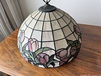 Tiffany style stained glass dome lampshade with pink tulip floral design on white background, viewed from the side on a wooden surface.