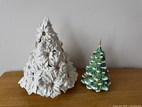 White ceramic Christmas tree with floral texture and light-up feature next to smaller green ceramic tree with colorful painted lights.