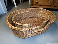 Two oval wicker pet beds showing different angles, basket weave construction and side handles.