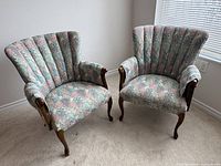 Pair of upholstered wing back chairs with floral leaf patterned fabric, wooden legs and arms visible. Shows overall style and condition.