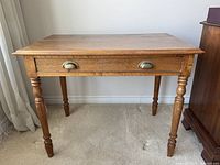 Front view of wooden table showing drawer and turned legs