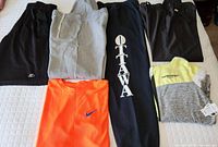 Photo of all apparel items laid out on a white bed surface, showing six pieces including pants, shorts, t-shirt and hoodie jacket.