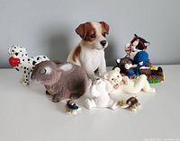 Photo displaying a collection of 12 animal figurines: two dogs (Dalmatian with red ball and brown/white puppy), brown bunny, two white bears, two cats (one colorful with hats, one white lying down), and four small turtles.