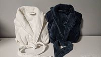 Two bathrobes folded, one white textured, one dark navy plush
