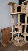 Photo showing the beige cat tree with multiple platforms and an attached cubby hole, along with a vertical sisal scratching pad with wooden base.