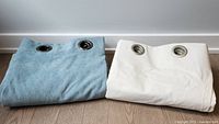 Turquoise soft microsuede curtain panel and white blackout curtain liner folded, showing metal grommet rings for hanging.