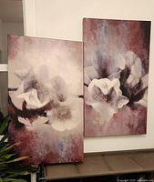 Two floral canvas artworks leaning side by side showing abstract flowers in muted colors with burgundy background.