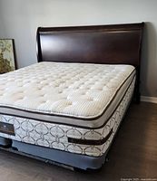 King size mattress on bed frame with dark wood headboard in room with wood floor and light walls.