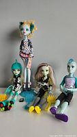 All four Monster High dolls standing and seated, showing full outfits and accessories including combs and stands