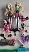 All four Monster High dolls, two standing with accessories and two lay down with more accessories in front
