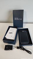 Samsung Galaxy S3 smartphone in blue inside the original box along with user guide and charger with cable laid out beside the box.