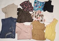 All ten tops laid out on bed showing variety of colors, patterns and styles including floral, tropical print, solid knit, and lace designs.