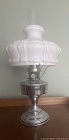 Full view of antique oil lamp showing metal base, burner and ornate white glass shade with clear glass chimney