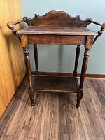 Front angle view of the antique wash stand showing turned legs, side towel racks, lower shelf, and shaped back panel.
