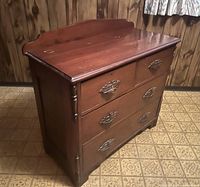 Front angled view of antique wood dresser showing four drawers with carved wooden handles and decorative side detailing.