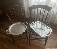 Two antique wooden chairs with metal serving trays resting on seats placed on wooden floor near curtain