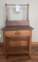 Front view of wooden antique washstand showing drawer with brass handle and cabinet door with carved decorative motif.