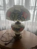 Full view of the glass table lamp showing fruit pattern, electrical cord, and ornate base