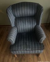 Front view of the vintage upholstered arm chair showing striped blue fabric upholstery and padded seat and backrest.