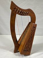 Front view of the small wooden lily harp showing its curved frame, carved decorative panel on the sound box, and eight nylon strings.