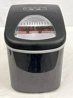 Front view of the black Frigidaire portable ice maker with clear lid and visible control panel area.