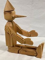 Full side view of the articulated wooden Pinocchio figure sitting, showing natural wood grain and joint construction.