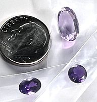 Close-up photo showing three loose faceted amethyst gemstones of varying sizes next to a dime for size comparison.
