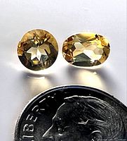 Two loose faceted citrine gemstones placed above a dime for size reference.
