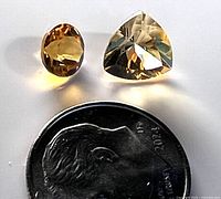 Two loose citrine gemstones—one oval and one trillion cut—shown beside a dime for size comparison.