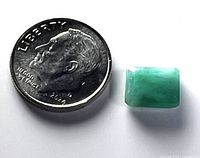 Photo showing a loose rectangular emerald gemstone placed next to a 2014 US dime coin for scale and comparison, well-lit on a white background.