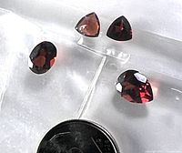 Four loose garnet gemstones with faceted cuts shown next to a dime for size comparison, on a white textured background.
