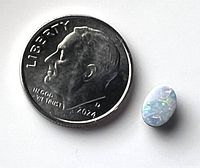 Photo showing an oval opal gemstone beside a 2014 dime for size reference.