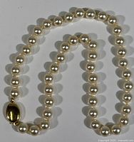 Full view of pearl necklace laid out, showing pearl strand and gold-tone clasp.