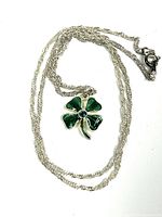 Full view of the necklace laid out showing the green enameled four leaf clover pendant and silver chain.