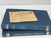 Stack of two hardcover books with a worn War Ration Book Four on top, focusing on spines showing titles and item surfaces.