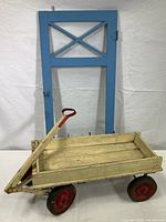 Full view of the blue painted wooden cabinet door with glass pane and the vintage child's wagon in front of it.