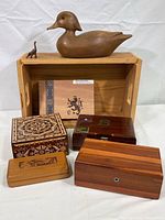 Photo showing the 13-inch carved wooden duck decoy, small anteater figurine, four wooden cigar boxes, and the large wooden storage box behind them.