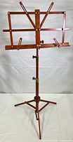 Full front view of assembled wooden sheet music stand with adjustable arms and tripod base.