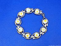 Close-up of the bracelet showing the raised daisy flower with white petals and yellow centers, silvertone leaf accents, and clasp.