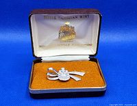 Brooch displayed inside original leather case with orange velvet cushion and white satin lining, showing Royal Canadian Mint logo inside lid