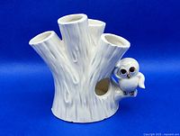 Front and side views of the white ceramic toothbrush holder shaped like a tree stump with five openings and a small owl figure attached.
