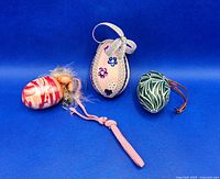 Three Easter egg ornaments on blue background: dark green wooden with white design, pink wooden with flowers and ribbon, and pink marbled plastic with tassel