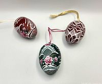 Three handpainted wooden Easter egg ornaments displayed together on a white surface, showing their size and design variety.