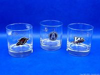 Front view of three Crown Royal whisky tumblers with logos of Calgary Stampeders, Toronto Argonauts, and Saskatchewan Roughriders on clear glass.