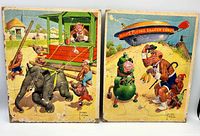 Front view of two vintage Lawson Wood chimpanzee family board puzzles with colorful animations, one showing an elephant being led by chimpanzees and the other a mars flying saucer theme scene.
